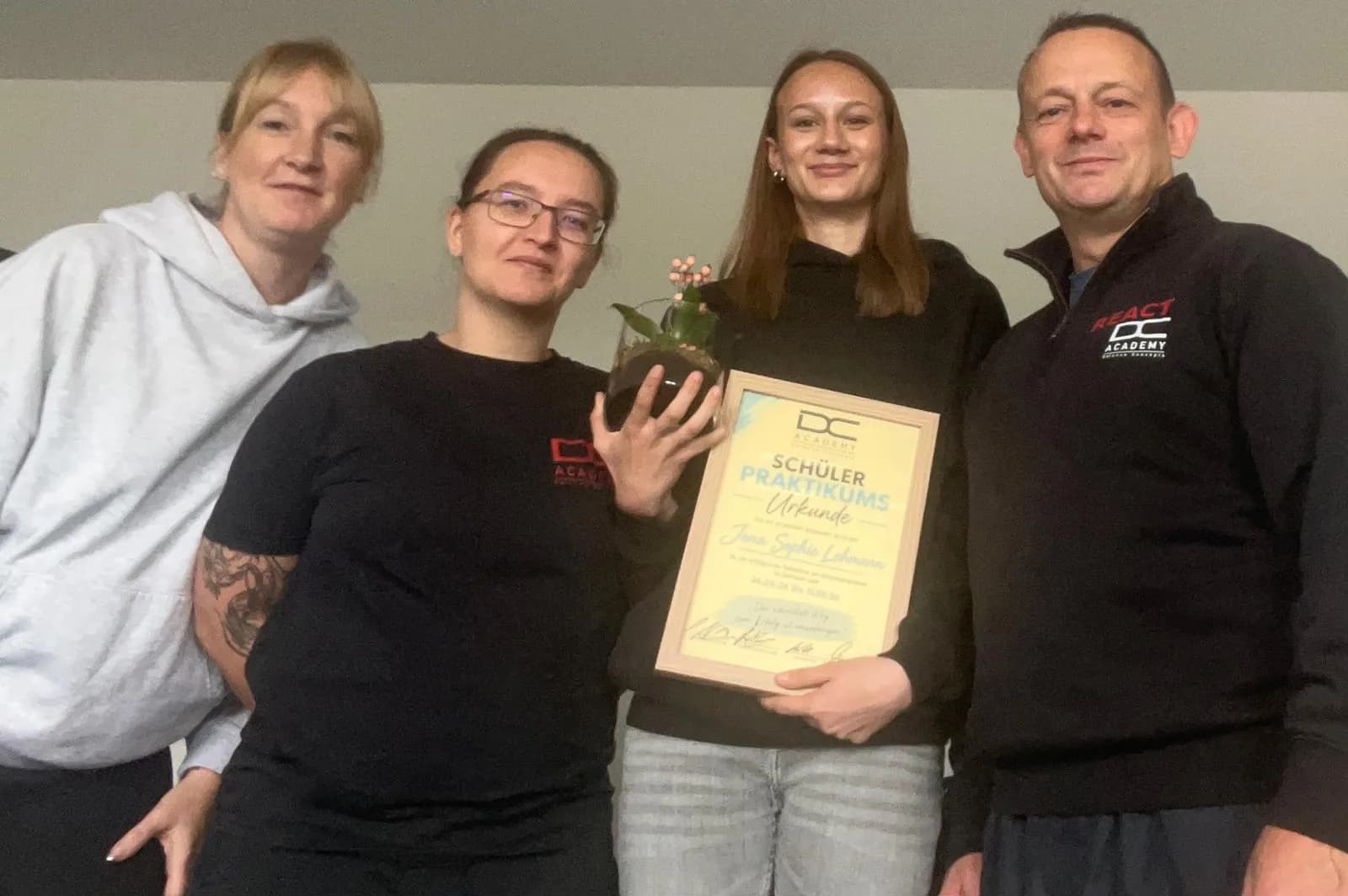 Abschluss eines Schülerpraktikums: Praktikantin mit Urkunde und Blumengeschenk, umringt vom Team der DC Academy